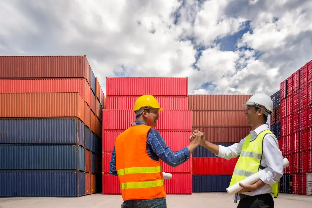 Two logistics professionals discussing Thailand import tax at a shipping container yard.