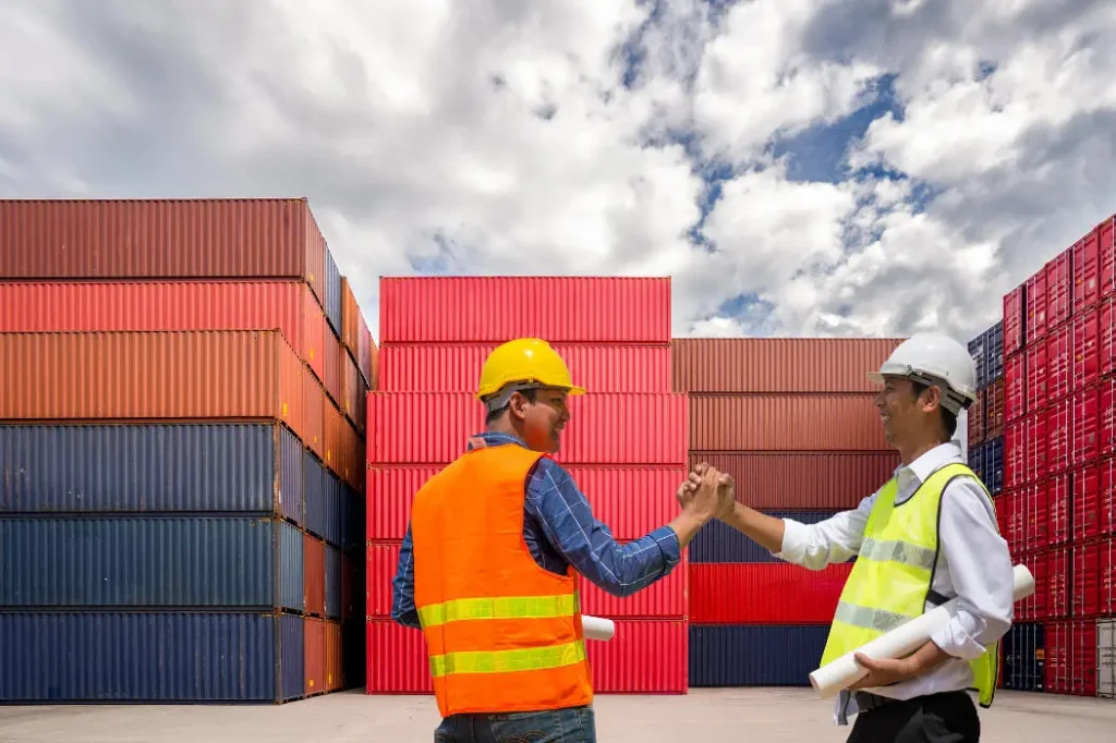 Two logistics professionals discussing Thailand import tax at a shipping container yard.